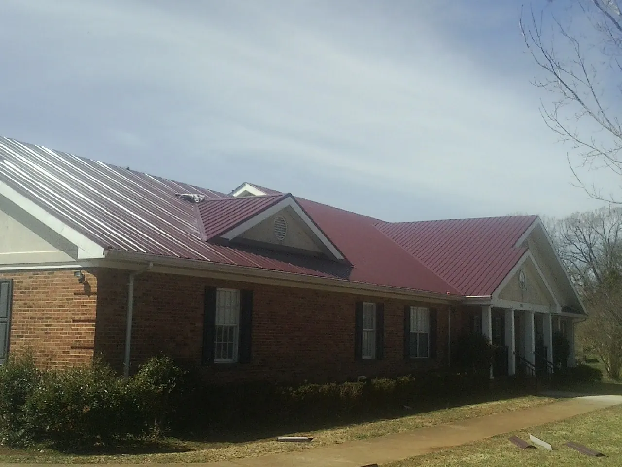 Red metal roof with gabled entries on a long brick building, from a Hail Damage Roof Repair job in Duncombe