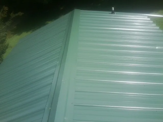 New green metal panels meeting at the ridge of a roof — Flat Roof Repair work by our crew in Duncombe