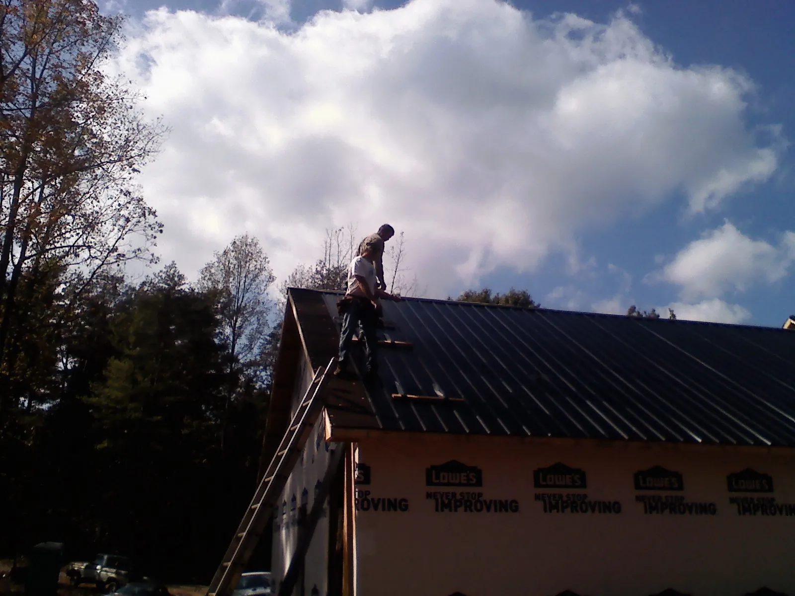 Roofer fastening dark metal panels high against a cloudy sky, from a Roof Inspection job in Duncombe