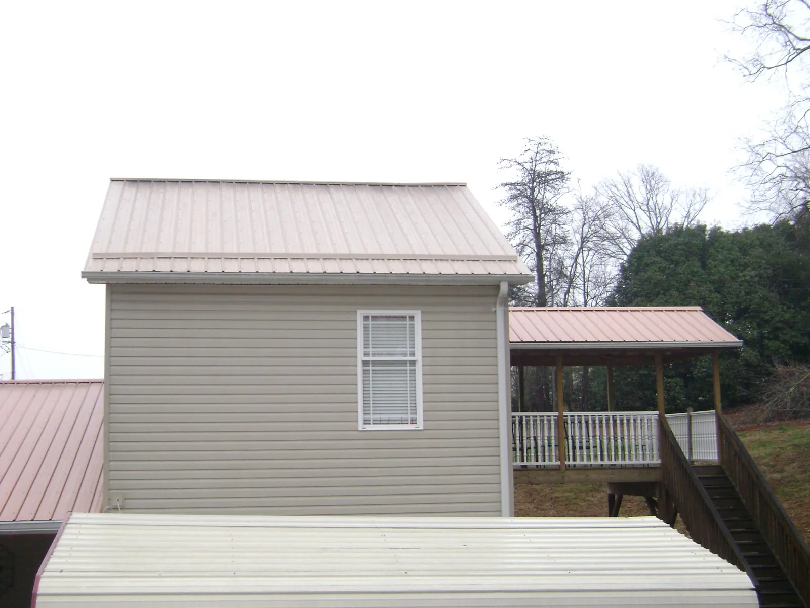 Tan metal roofs on a two story addition and attached porch, from a Roof Replacement job in Duncombe